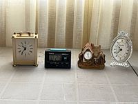 Four clocks: brass Envoy carriage, Timex digital, cottage resin analog, oval clear resin analog