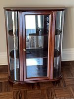 Front view of wood and glass wall curio cabinet showing glass door and curved glass sides