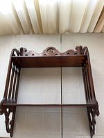 Front view of two-tier wood shelf showing scroll crest and shelves