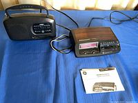 Both GE radios side by side with cords visible and manual in foreground