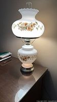Full view lamp illuminated on table showing floral design and shape