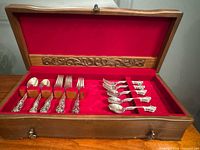 Open wooden chest showing flatware pieces inside red velvet lining