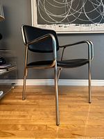 Three-quarter side view of chair showing chrome tubular frame, arms, legs, black seat and back