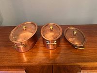 Three copper pots with lids displayed