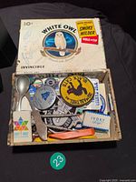 Open White Owl cigar box filled with assorted small collectibles, patches, spoon, soap