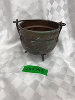 Front view of copper pot showing tripod legs, handle mounts, verdigris patina