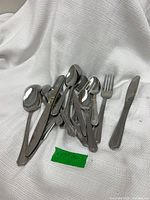 Pile of various stainless steel flatware pieces on white cloth