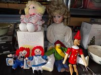 Group shot of all dolls including Precious Moments box, Raggedy Ann & Andy, Pinocchio, Henry Curtis doll body and Armand Marseille bisque doll