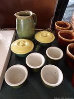 Group shot showing pitcher, two crock lids, four cups and brown crocks