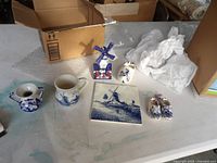 All six Delft Blue items displayed: ashtray, mug, tile, windmill figurine, clogs, pitcher