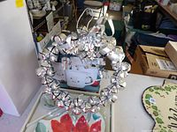 Silver jingle bell wreath with ribbon; boxes of Pfaltzgraff items visible