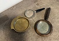 Overview of all three items: brass coin tray, metal magnifier, wooden-handle magnifier