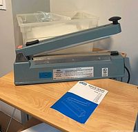 Full view of Uline impulse sealer with manual and bin of plastic bags