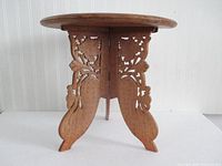 Side view of carved teak folding table showing intricate openwork base