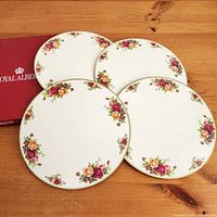 Four round Old Country Roses placemats and worn red Royal Albert box displayed on wooden surface