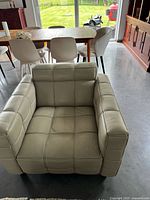 Front angle of light beige leather armchair showing stitched square pattern, wide arms, and deep seat