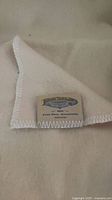 Close-up of woven label on cream wool blanket showing MacAusland’s Woollen Mills branding and whipstitched edge
