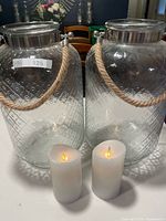 Two textured glass hurricane candle holders with rope handles and two LED candles front view