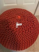 Top view of one burnt orange knitted pouf ottoman showing knit texture and color