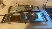 Two electric warming trays with three stainless dishes on top