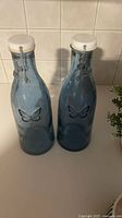 Two blue glass swing-top bottles with butterfly design