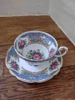Top view of saucer and cup showing floral and blue scroll pattern with gold trim