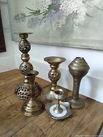 Five assorted brass candlesticks on wooden surface