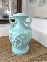 Front view of mint-green ceramic lamp body showing handles and floral relief