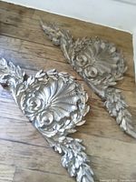 Both resin pediments showing front relief details and size perspective on wood floor