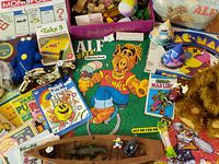 Close-up center highlighting ALF coloring book, Pac-Man book, plush figures, wooden canoe