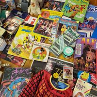 Overall spread of books, comics, cassettes, plush, Spider-Man sweatshirt and Superman record