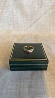 Ring on closed dark green jewellery box showing front view with pink sapphire