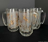 Three frosted glass beer mugs showing pinecone motifs and handles