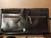 Front view of handbag showing two zippered pockets, leather finish, flap design