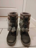 Front view of both boots showing toe, faux-fur collar, knit cuff, laces with pom-poms