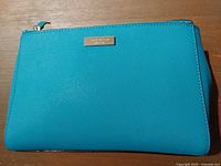 Front view showing turquoise saffiano-style exterior and gold-tone logo plate