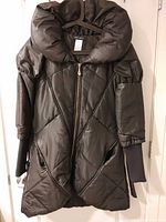 Front view of black quilted coat showing collar, zipper, pockets