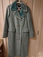Front view of long light blue faux-shearling coat hanging on door
