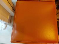 Top surface of orange vinyl ottoman showing condition and stitching