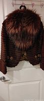 Front view of dark brown rabbit fur jacket with burgundy-brown fur collar hanging on door