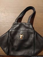 Front of black leather handbag with gold X logo and handles visible