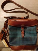 Front view showing plaid body, leather flap, buckle, strap
