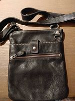 Front view showing full bag, exterior zip pocket, strap, leather texture, hardware