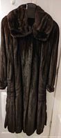 Front view of full-length dark brown mink coat on hanger showing overall design and length