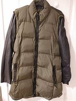 Front view of olive quilted puffer jacket with black faux leather sleeves and zip pockets