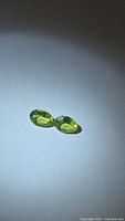 Pair of apple green oval peridots on neutral background