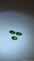 Three oval chrome diopside gemstones on neutral background