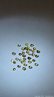 Group of approximately 35 small round yellow-green tanzanite stones on neutral background