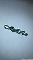 Four oval cut aqua green to blue sapphires aligned on white background