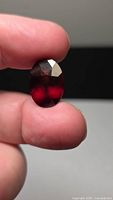 Faceted oval garnet held between fingers, front view shows color and facets